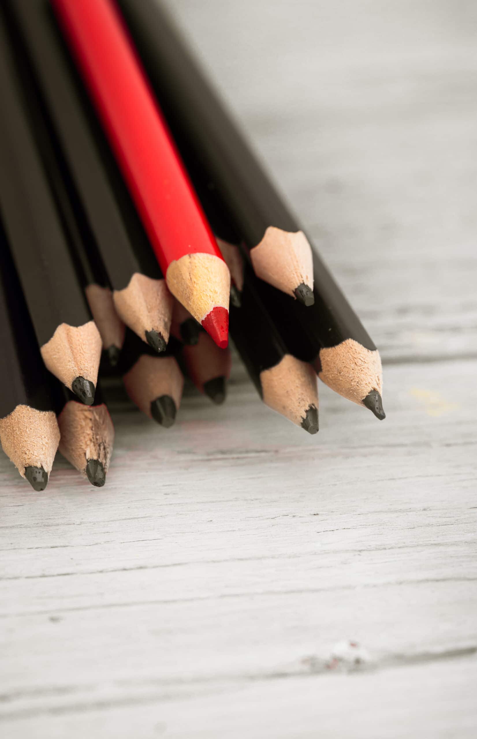 Red pencil stands out from the crowd of black on a wooden white background.